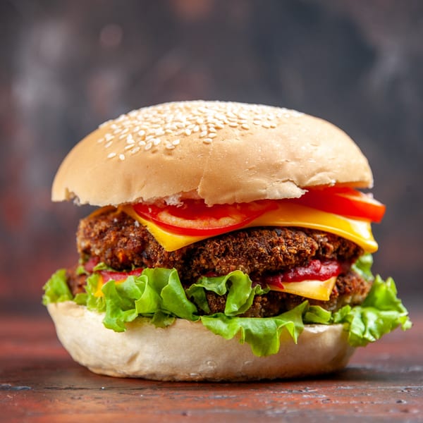 Close-up of a double patty burger with cheese, lettuce, tomato, and sesame seed bun.