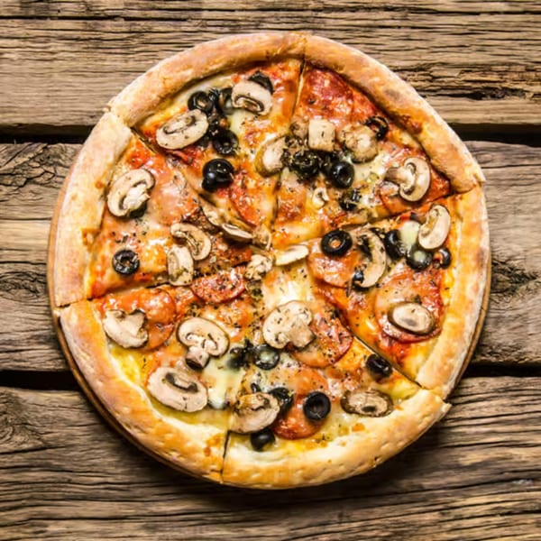 Round pizza with mushrooms, black olives, and pepperoni, sliced on a rustic wooden table.
