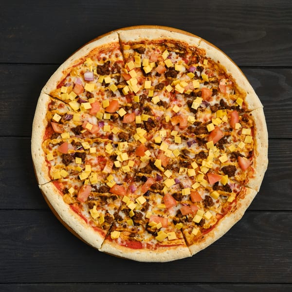 Overhead view of a whole pizza with ground meat, diced tomatoes, red onions, and cheese cubes.