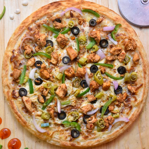 Overhead view of a chicken pizza with olives, green peppers, and red onions on a wooden table.