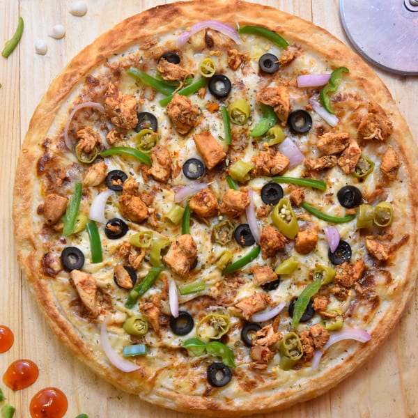 A chicken pizza with black olives, green peppers, and onions on a wooden table.