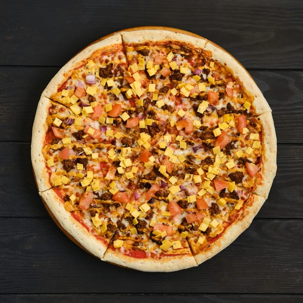 Overhead view of a sliced pizza with ground meat, diced tomatoes, red onions, and cheese cubes.