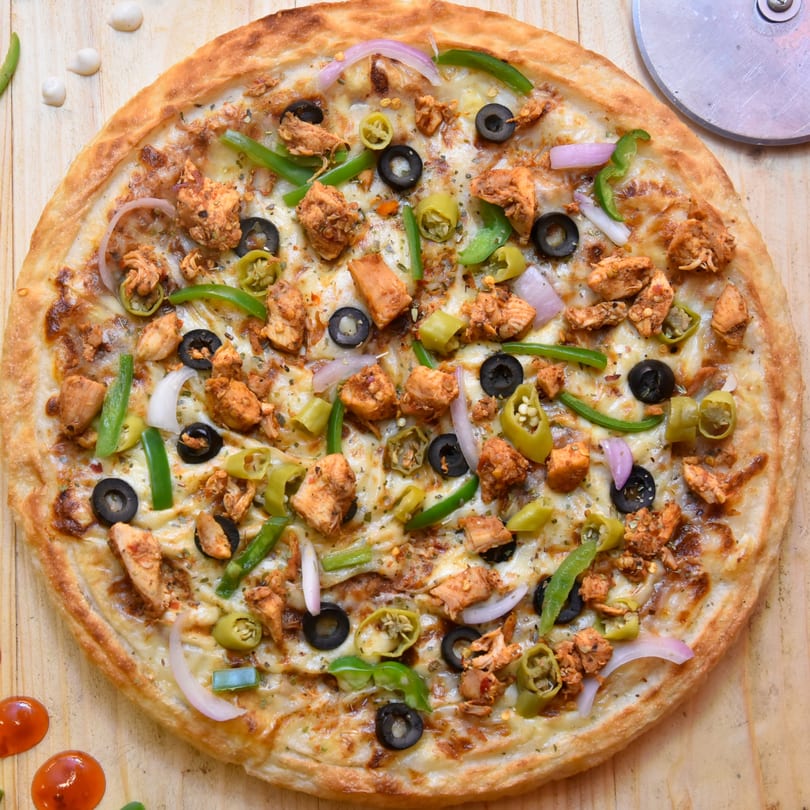 Chicken pizza with black olives, green peppers, onions, and cheese on a wooden table.