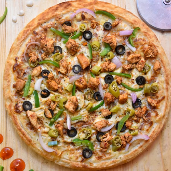 Chicken pizza with black olives, green peppers, and red onions on a wooden table.