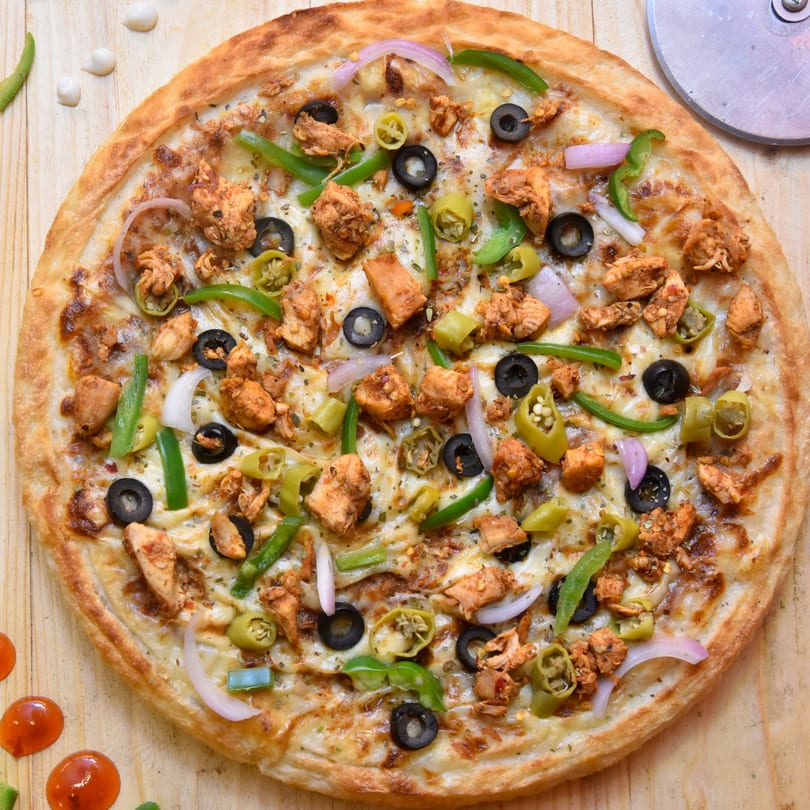 Chicken pizza with black olives, green peppers, and red onions on a wooden table.