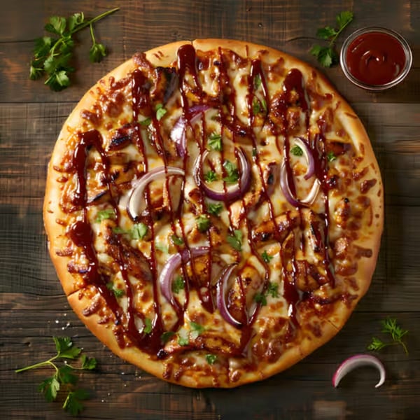 BBQ chicken pizza with red onions, cilantro, and a side of BBQ sauce on a wooden table.